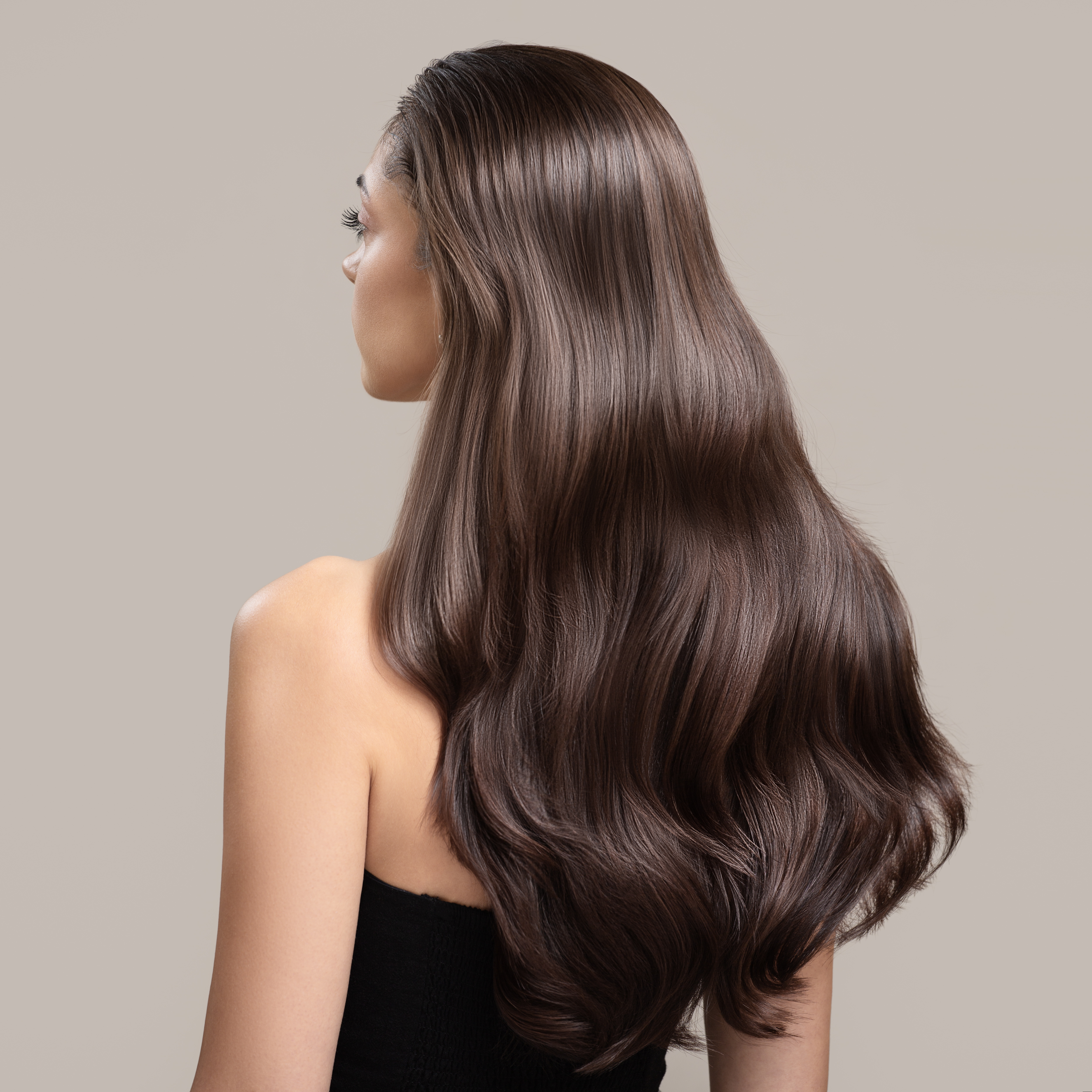 Kobieta stojąca tyłem z długimi, lśniącymi lokami w odcieniu chłodnego brązu