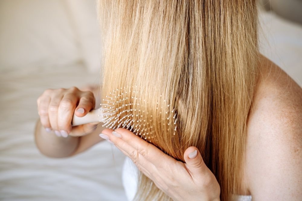 Kobieta z długimi, blond włosami rozczesuje włosy szczotką