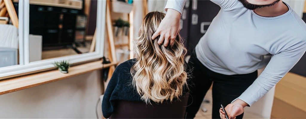 Fryzjerka układa blond włosy klientki w salonie fryzjerskim.