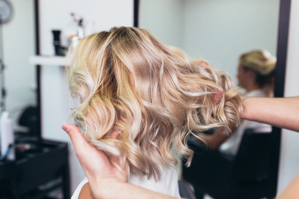 Fryzjerka w salonie przeczesująca klientce blond włosy do ramion z jaśniejszymi refleksami