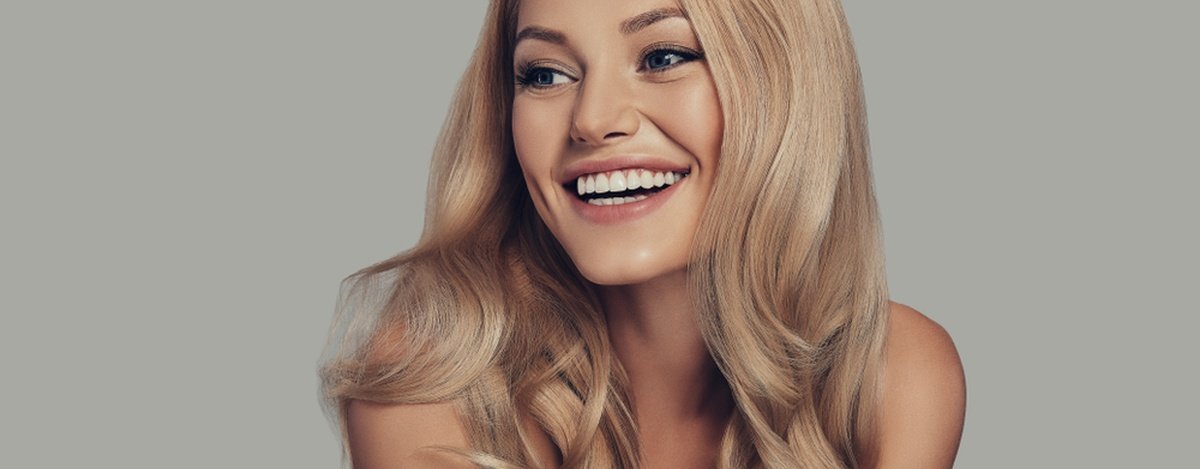 Uśmiechnięta młoda kobieta z lśniącymi blond włosami na szarym tle