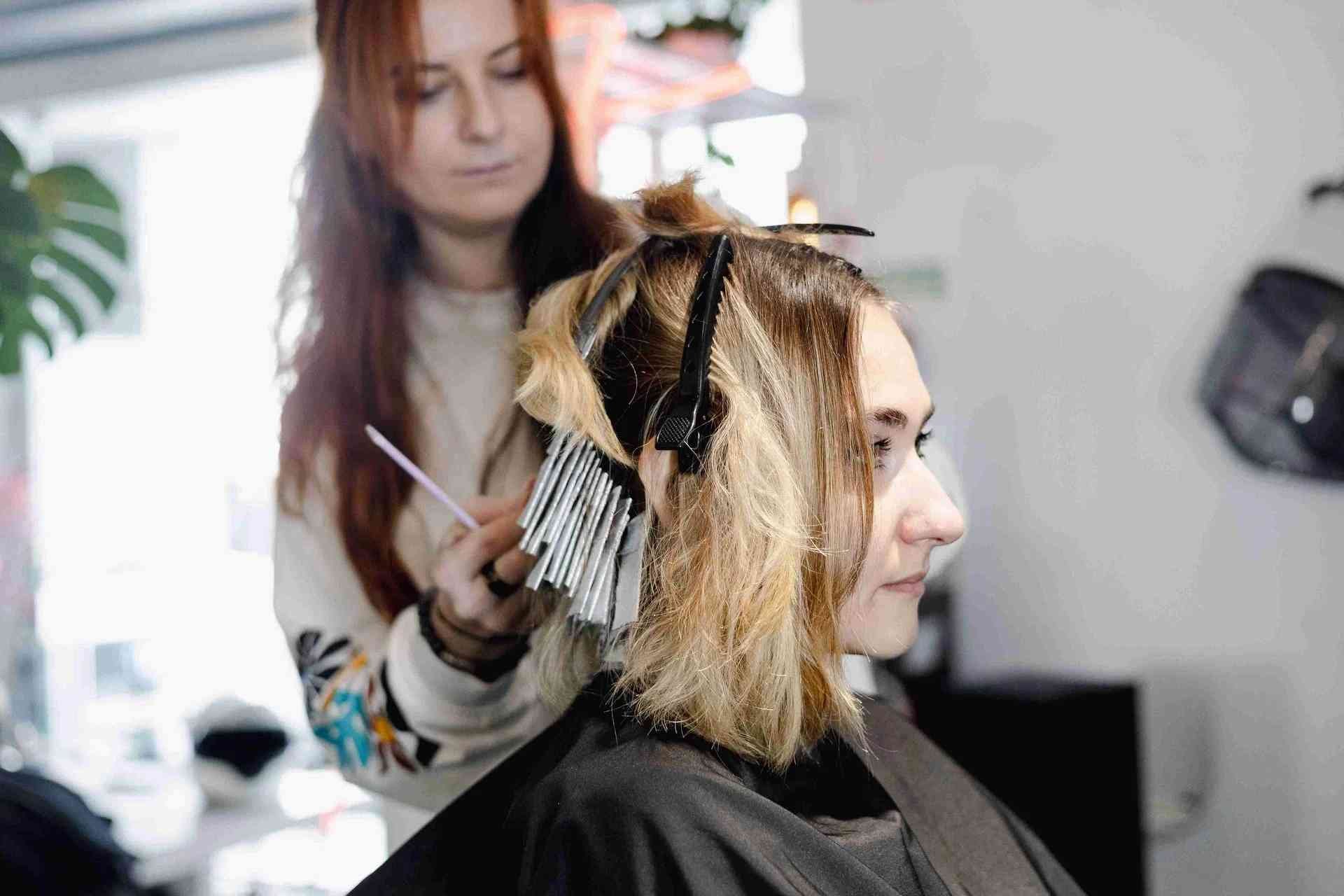 Fryzjerka farbuje włosy klientki w salonie, używając folii i pędzelka.