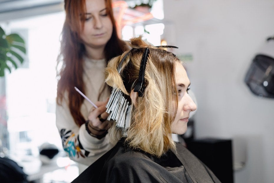 Fryzjerka farbuje włosy klientki w salonie, używając folii i pędzelka.