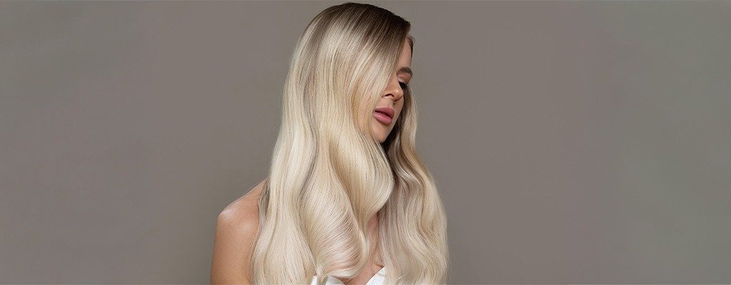 Blond kobieta z długimi włosami patrzy w dół na neutralnym tle.
