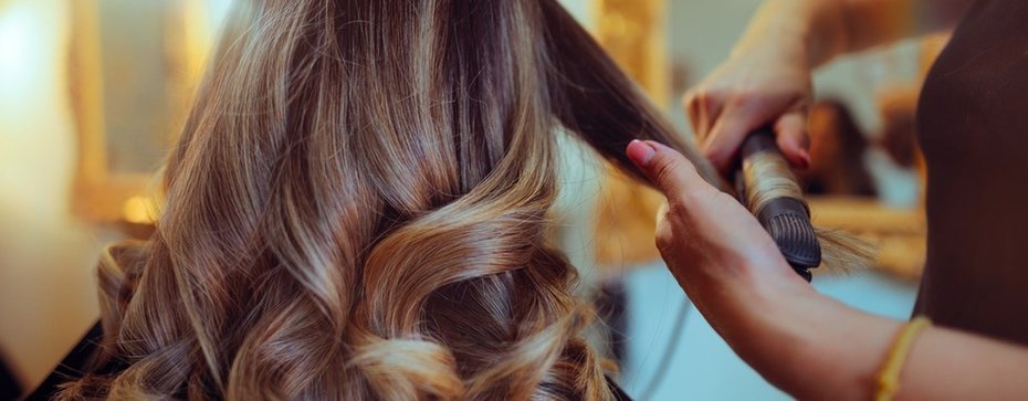 Fryzjerka stylizuje długie, falowane włosy w salonie fryzjerskim