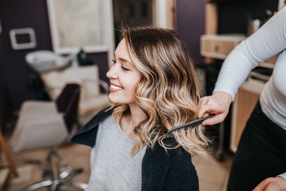 Fryzjer rozczesujący falowane blond włosy klientce podczas wizyty w salonie