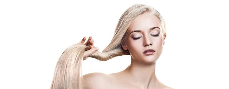 Blondynka z zamkniętymi oczami trzyma i przeciąga pasmo włosów na białym tle.