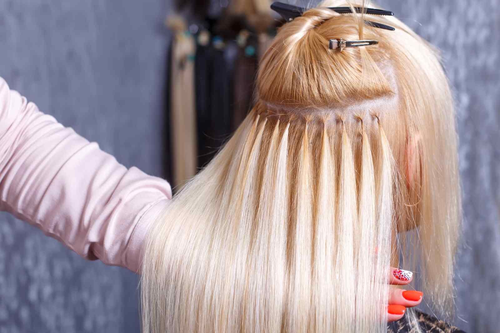 Blondwłosa kobieta podczas zabiegu przedłużania włosów w salonie fryzjerskim.