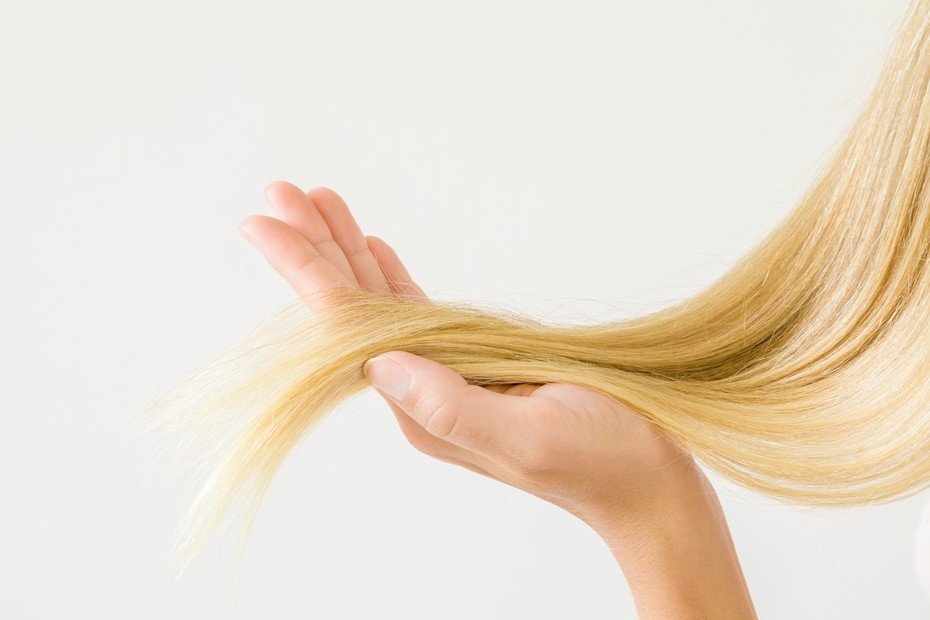 Dłonie trzymają i wygładzają blond pasmo włosów na jasnym tle.